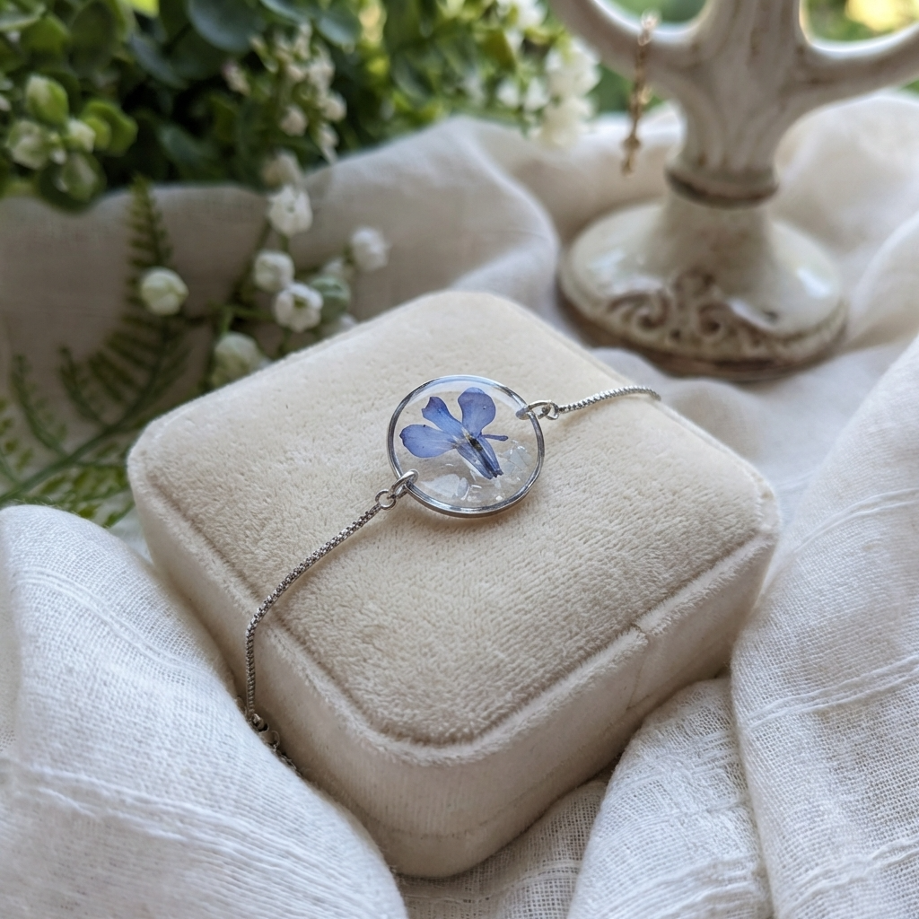 Platinum plated blue lobelia bracelet shown on a jewellery holder, crafted with garden grown flowers, resin and seashell flakes