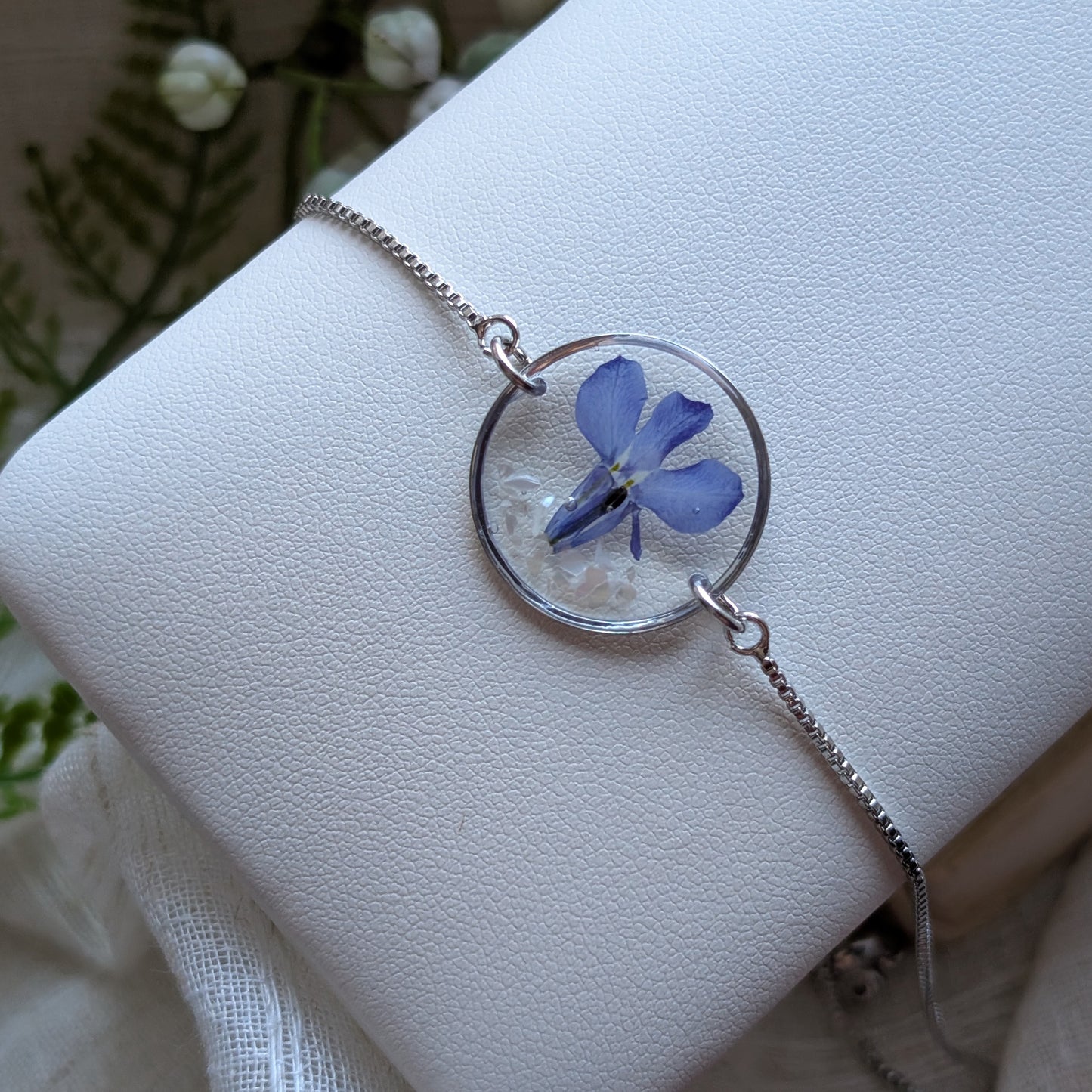 Blue lobelia 20mm flat bracelet with seashell flakes on jewelry display stand, handmade real flower jewelry by Work by Nature