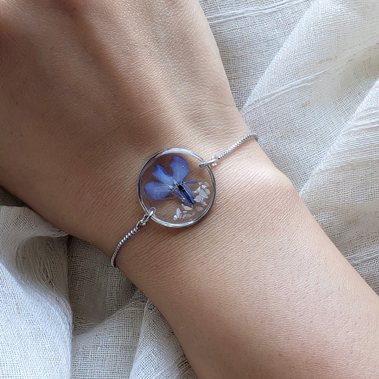 Model with fair skin wearing a blue lobelia 20mm flat bracelet, delicate platinum plated real flower jewellery for everyday wear
