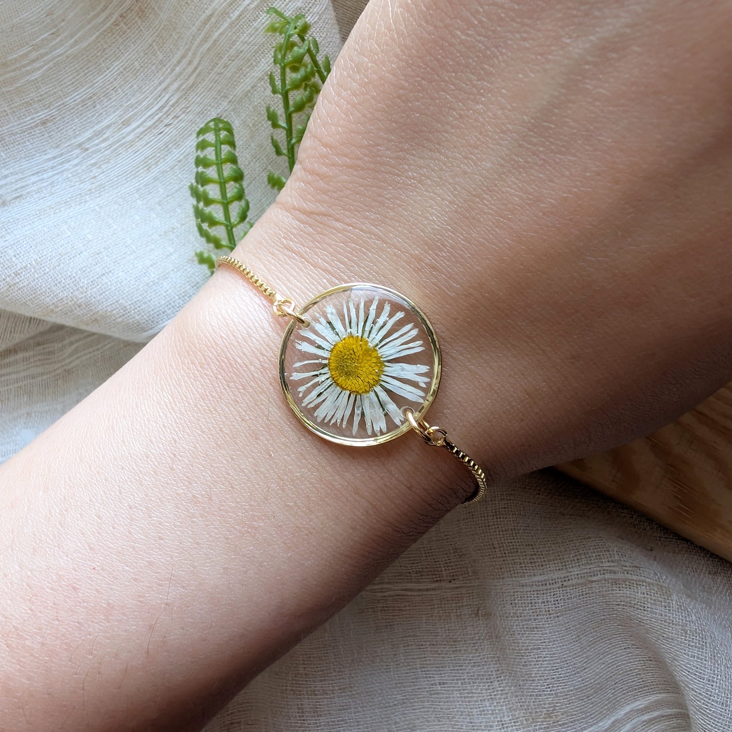 Model with fair skin wearing a daisy 20mm flat bracelet, delicate gold plated real flower jewellery for everyday wear
