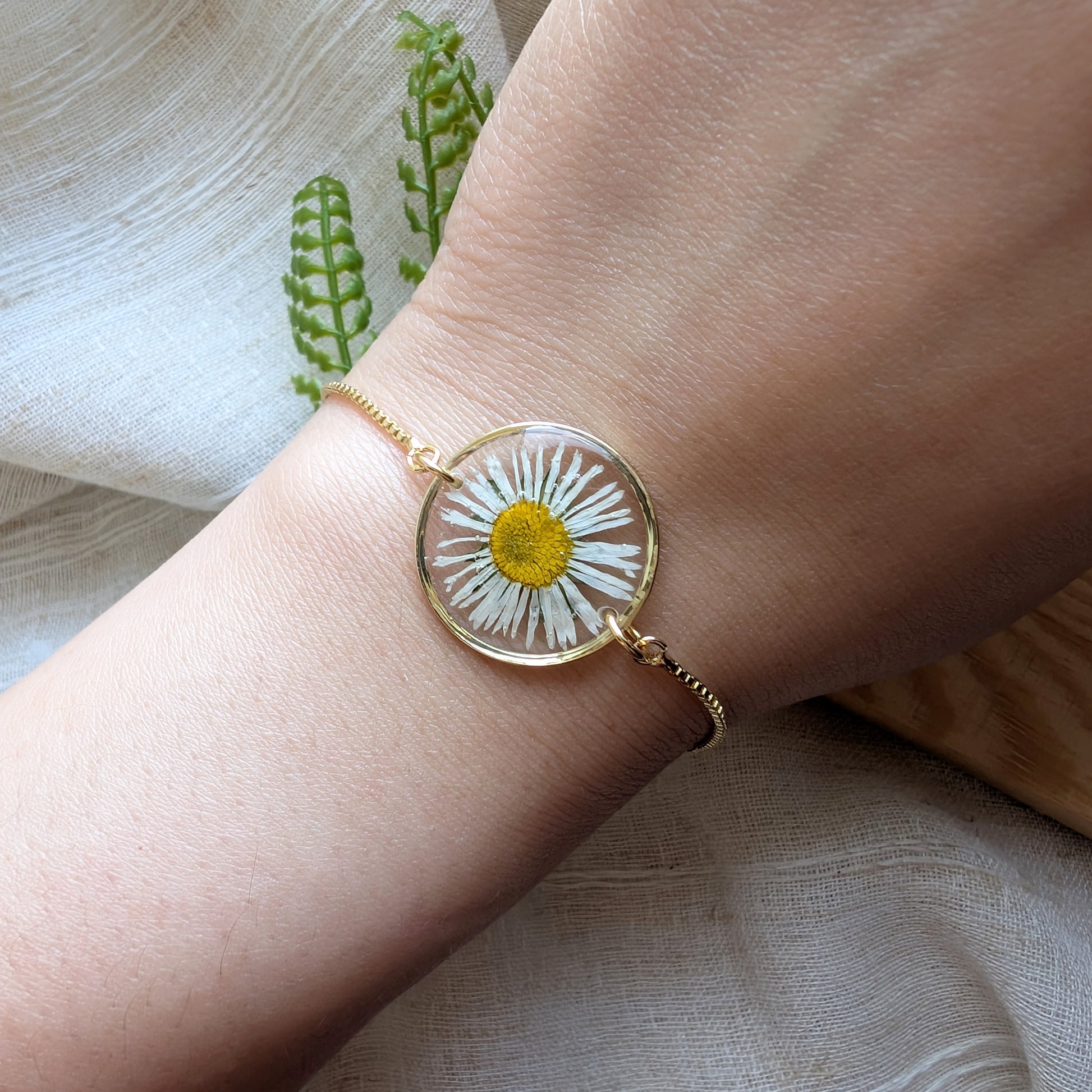 Model with fair skin wearing a daisy 20mm flat bracelet, delicate gold plated real flower jewellery for everyday wear

