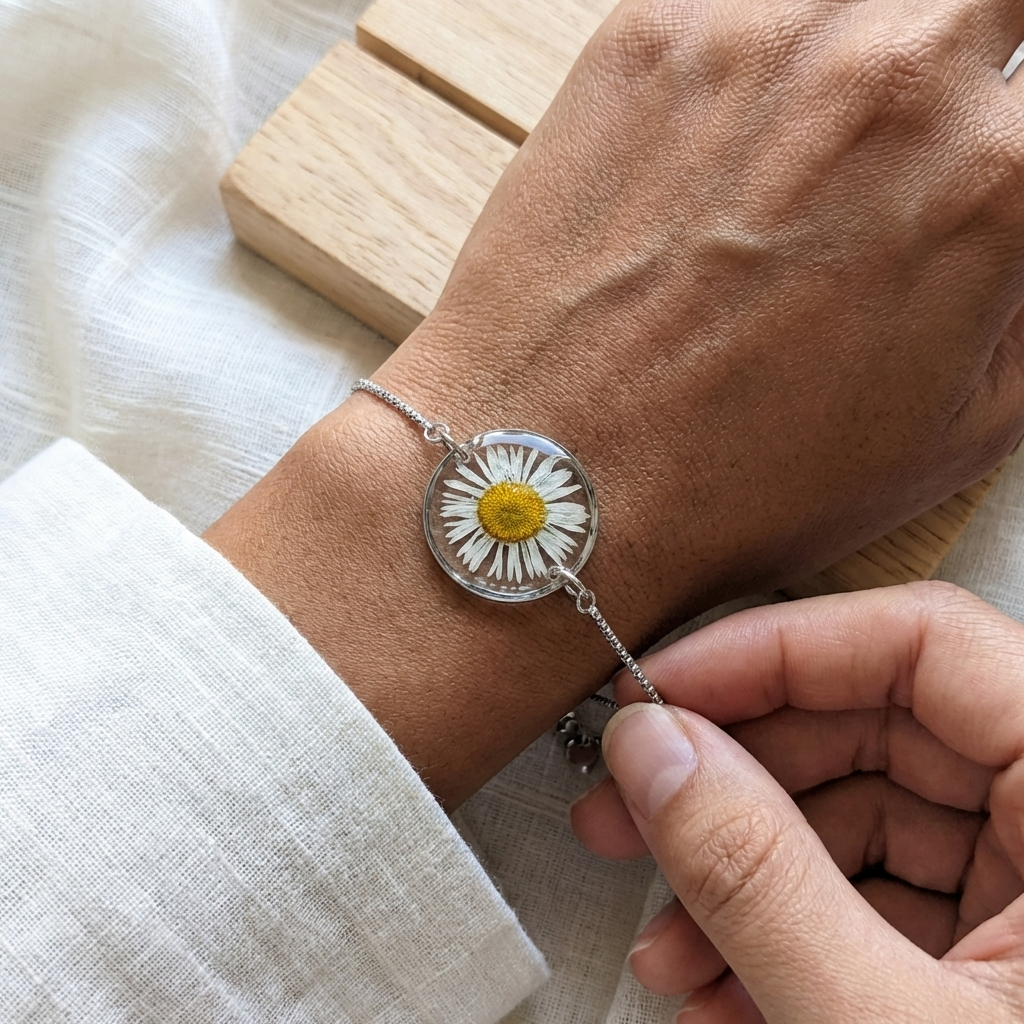 Hand wearing a silver bracelet with a daisy charm on a dark skin model