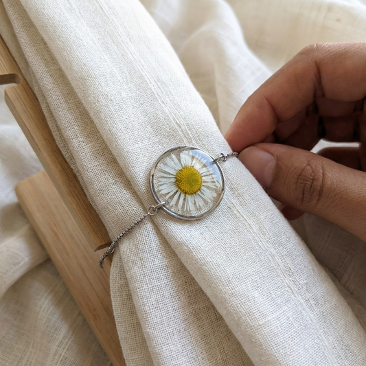 Hand holding a daisy floral pendant against a light fabric background