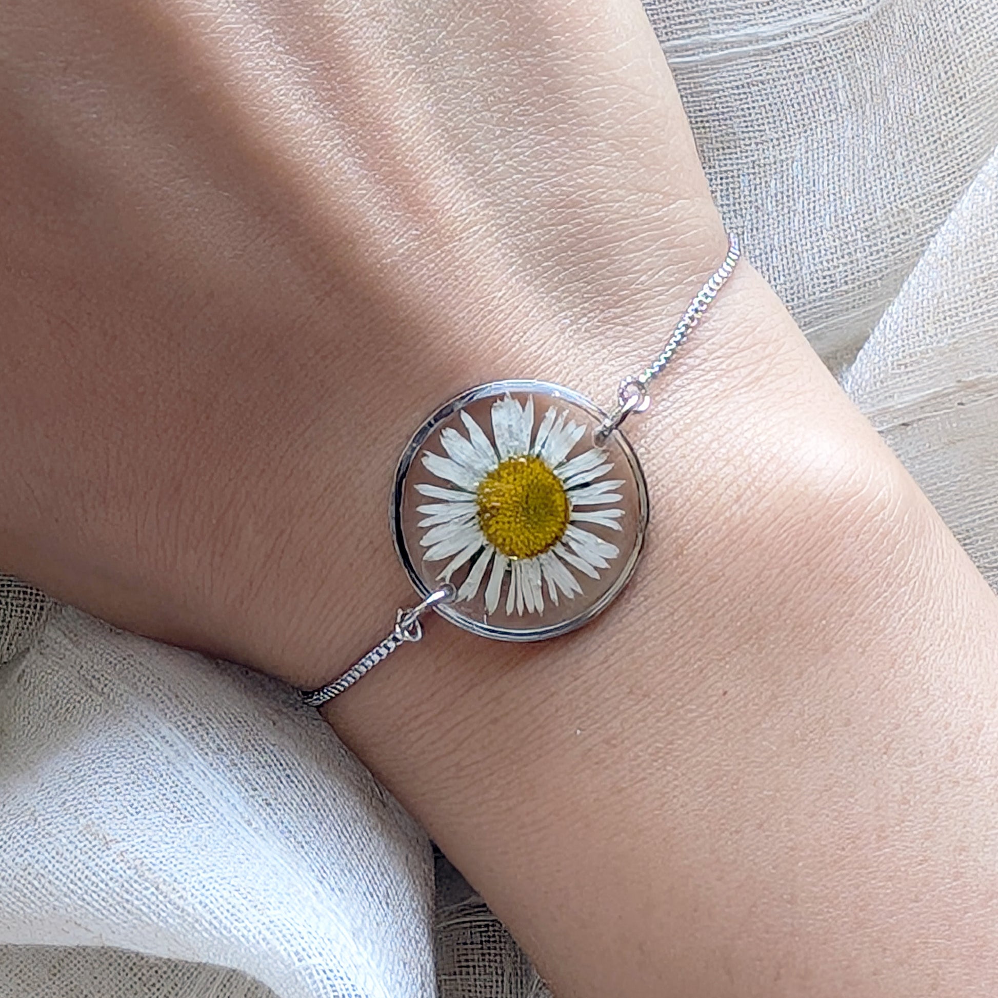 Bracelet with a daisy flower design on a wrist against a neutral background