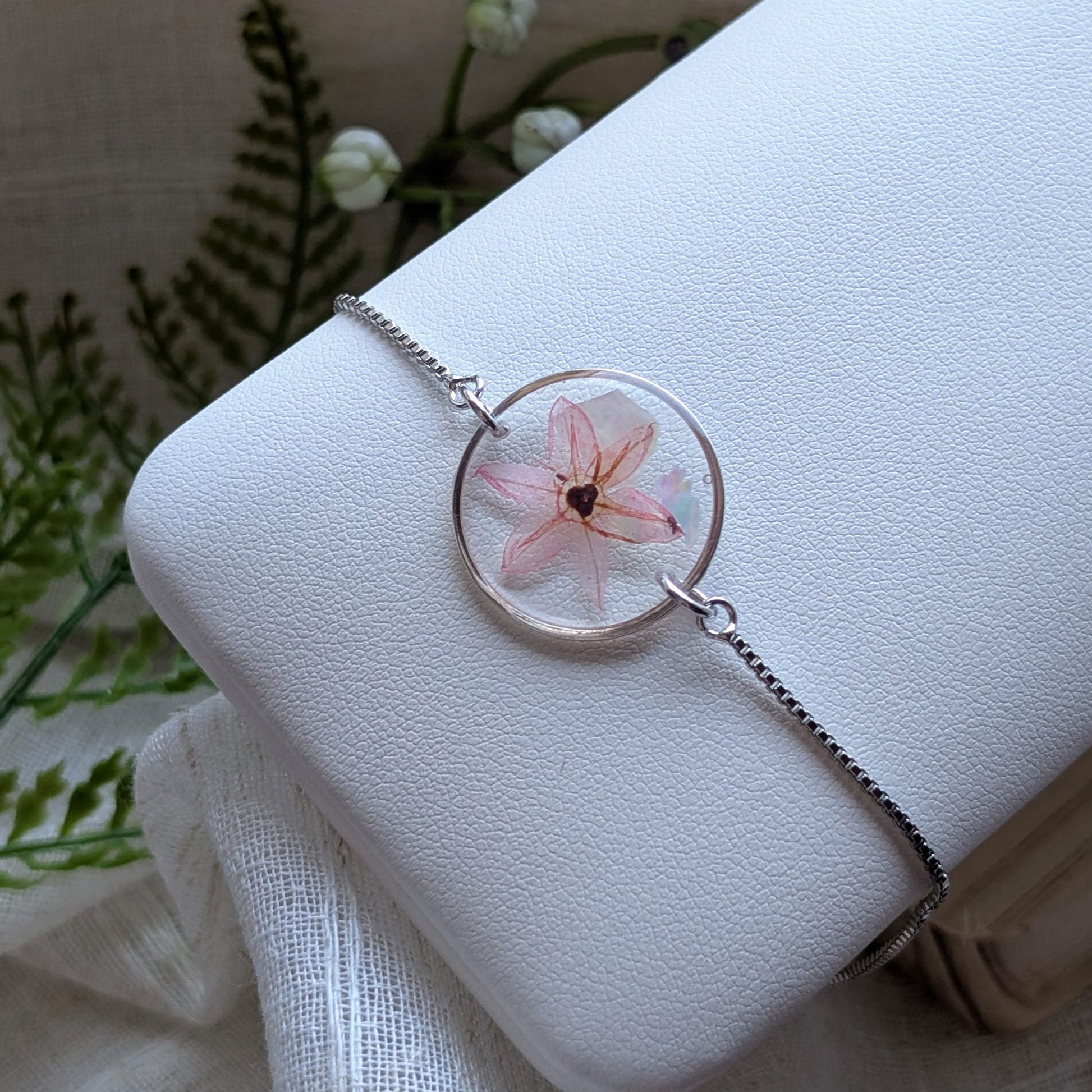 Platinum plated pink chive blossom bracelet shown on a jewellery holder, crafted with real flowers, resin and seashell flakes
