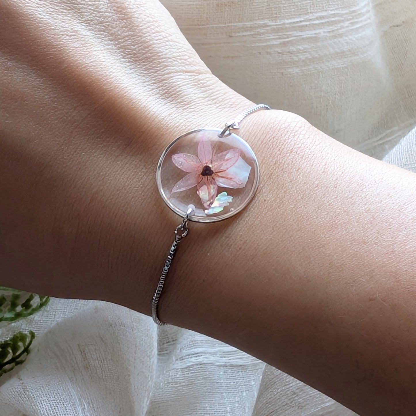 Model with fair skin wearing a pink chive blossom 20mm flat bracelet, delicate platinum plated real flower jewellery for everyday wear
