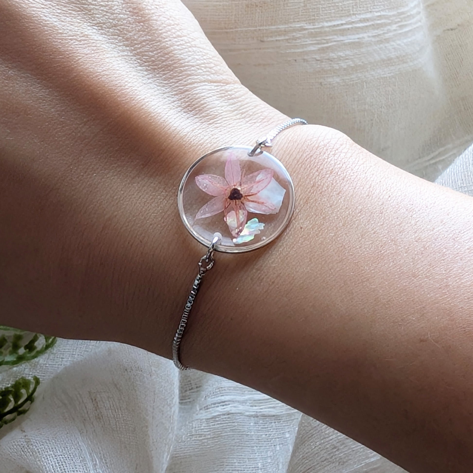 Model with fair skin wearing a pink chive blossom 20mm flat bracelet, delicate platinum plated real flower jewellery for everyday wear
