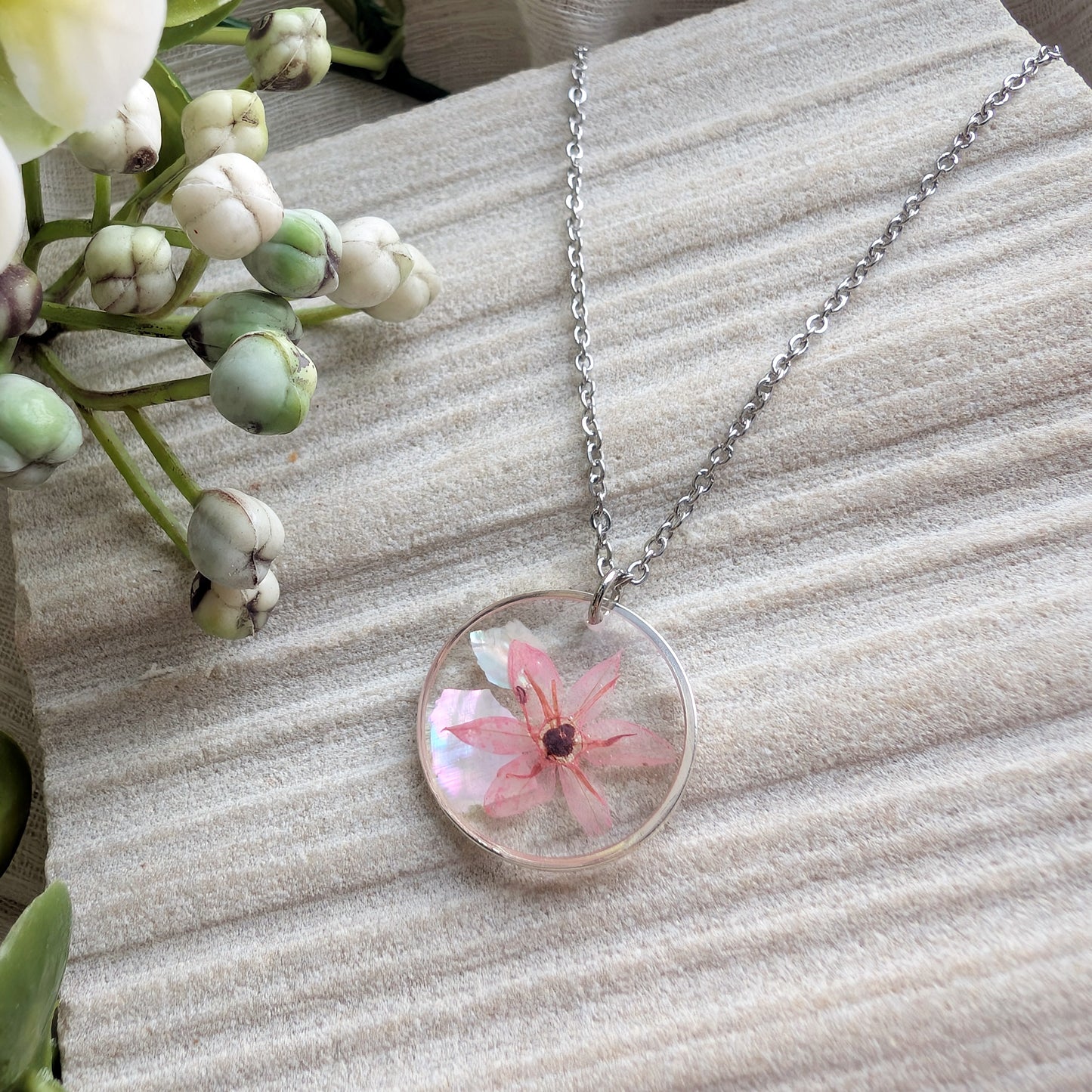 Stainless Steel pink chive blossom necklace shown on a jewellery holder, crafted with real flowers, resin and delicate seashell flakes
