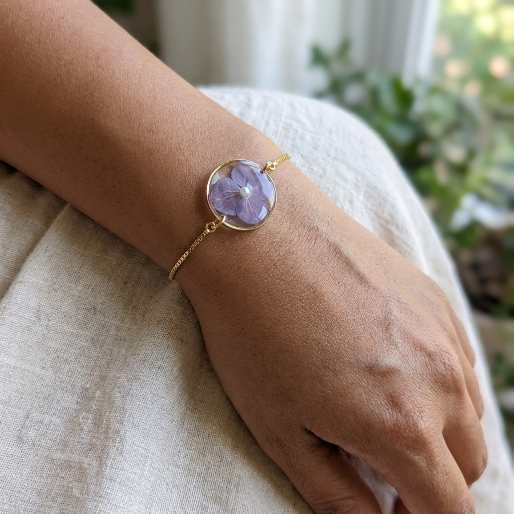 Dark skin tone model wearing a purple hydrangea bracelet, showing a soft contrast with delicate gold plated jewellery