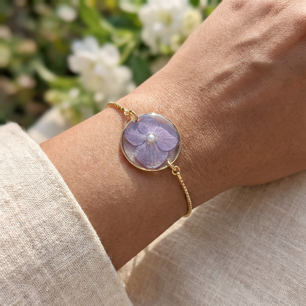 Gold bracelet with a purple flower charm on a wrist against a blurred natural background