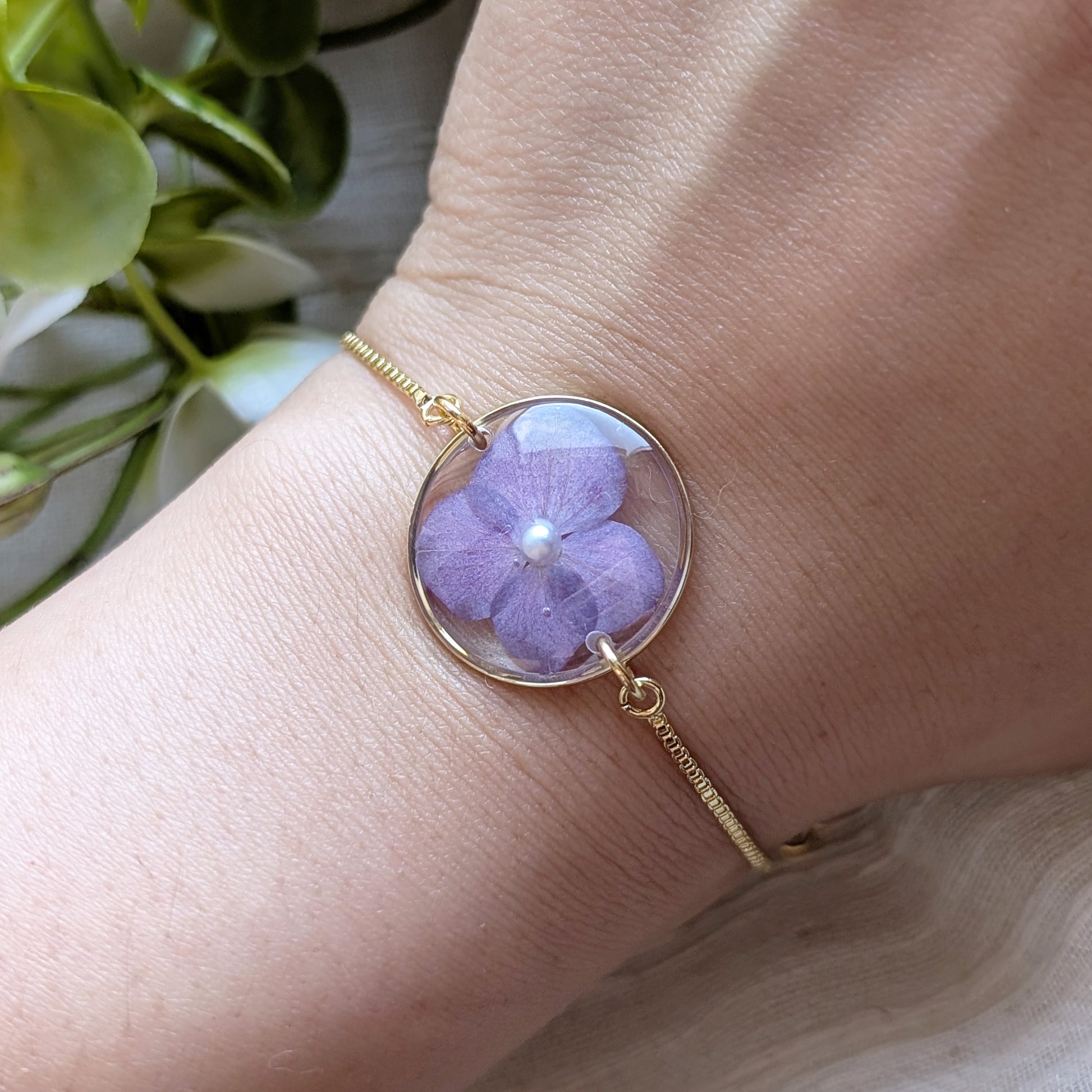 Model with fair skin wearing a purple hydrangea 20mm flat bracelet, delicate gold plated real flower jewellery for everyday wear