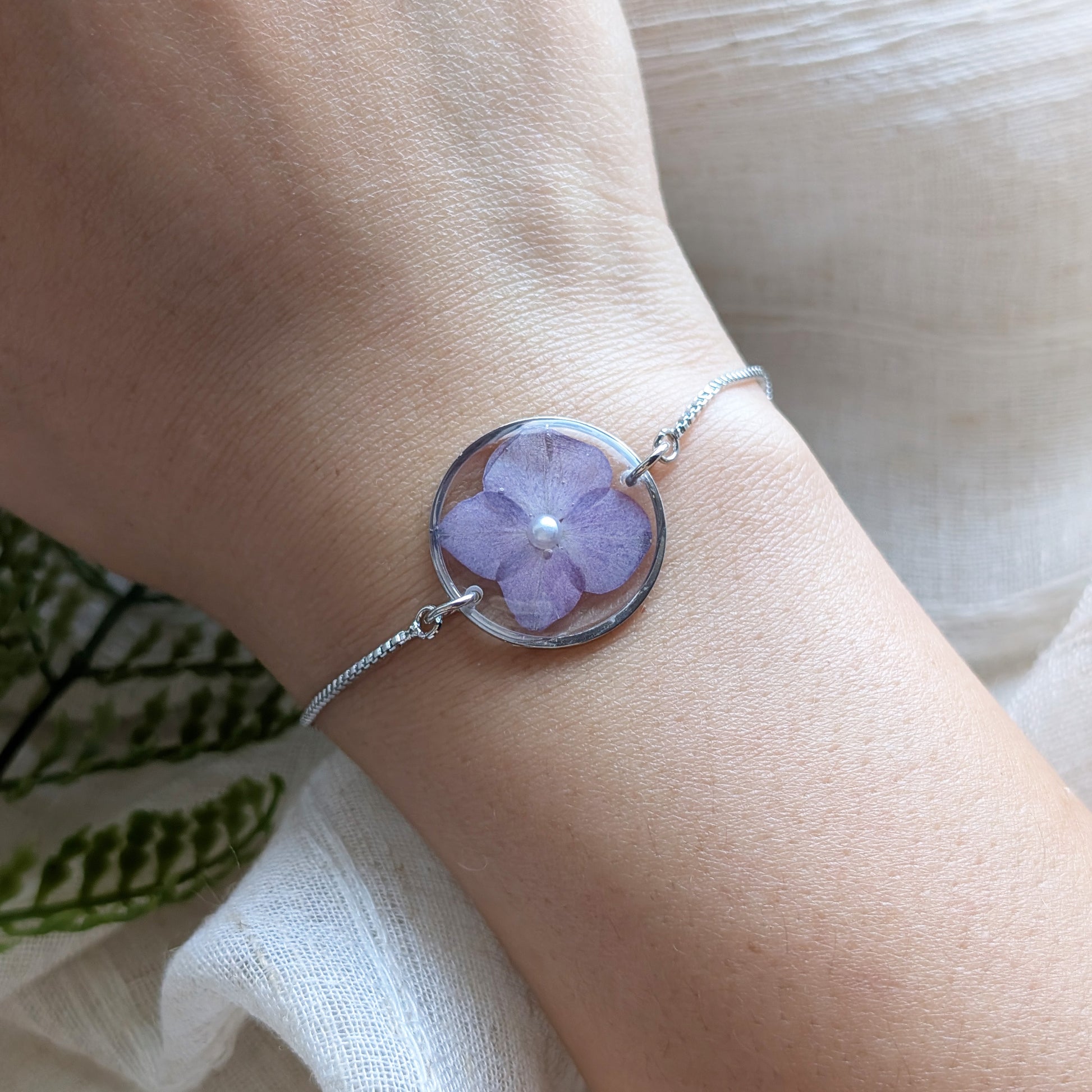 Model with fair skin wearing a purple hydrangea 20mm flat bracelet, delicate platinum plated real flower jewellery for everyday wear