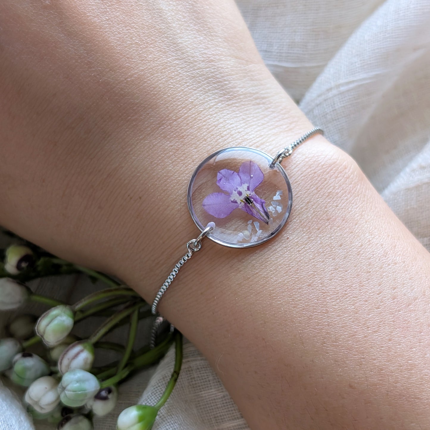 Model with fair skin wearing a purple lobelia 20mm flat bracelet, delicate platinum plated real flower jewellery for everyday wear