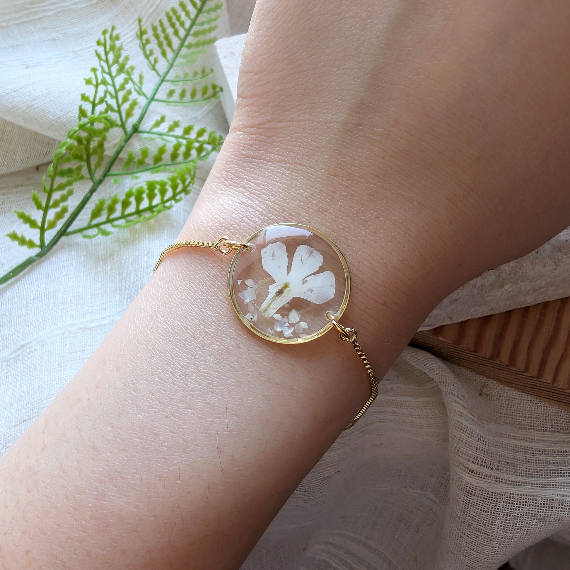 Model with fair skin wearing a white lobelia 20mm flat bracelet, delicate gold plated real flower jewellery for everyday wear