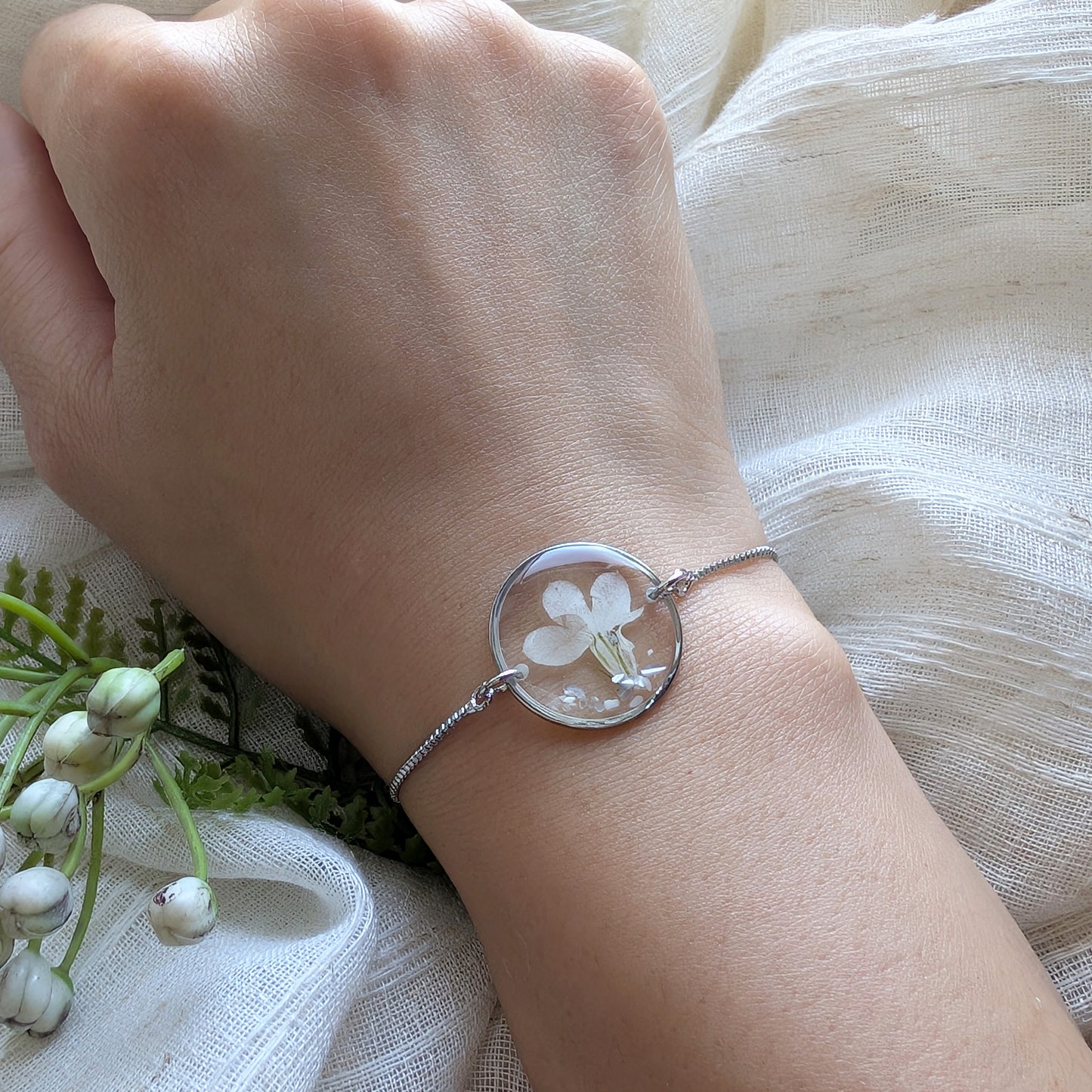 Model with fair skin wearing a white lobelia 20mm flat bracelet, delicate platinum plated real flower jewellery for everyday wear